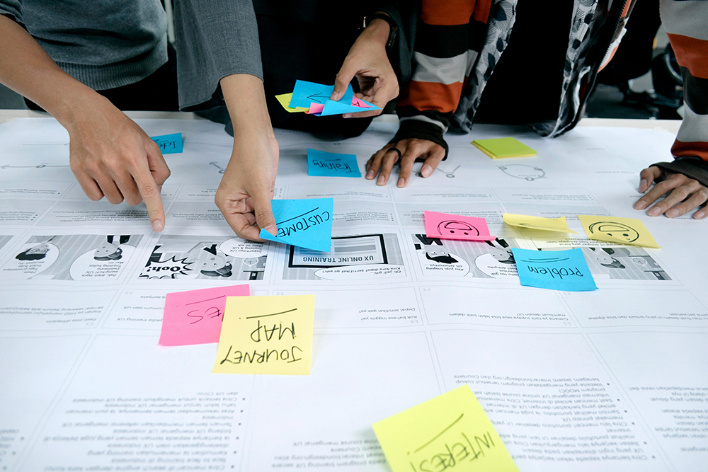 Group of colleagues gathered round a desk planning a digital product management project with post it notes and print outs
