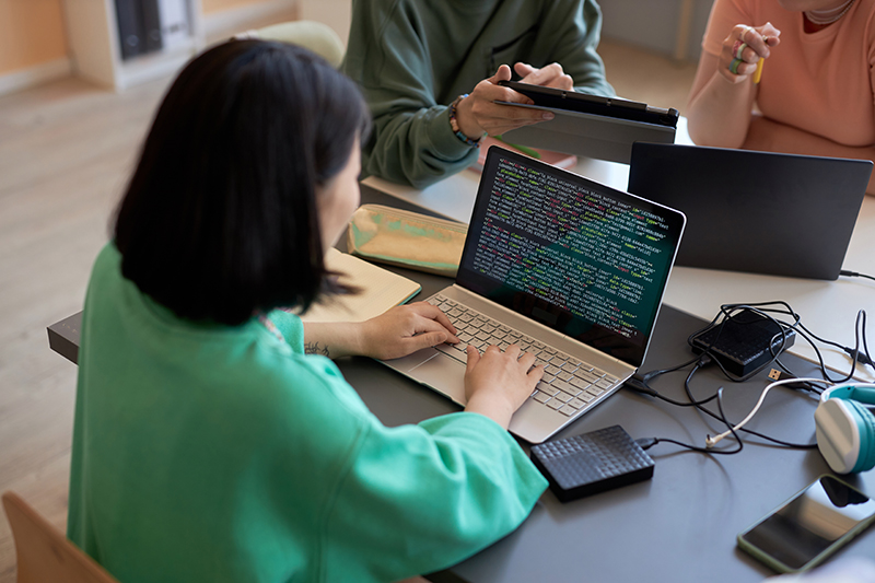 Woman in green jumper at a laptop with code on the screen